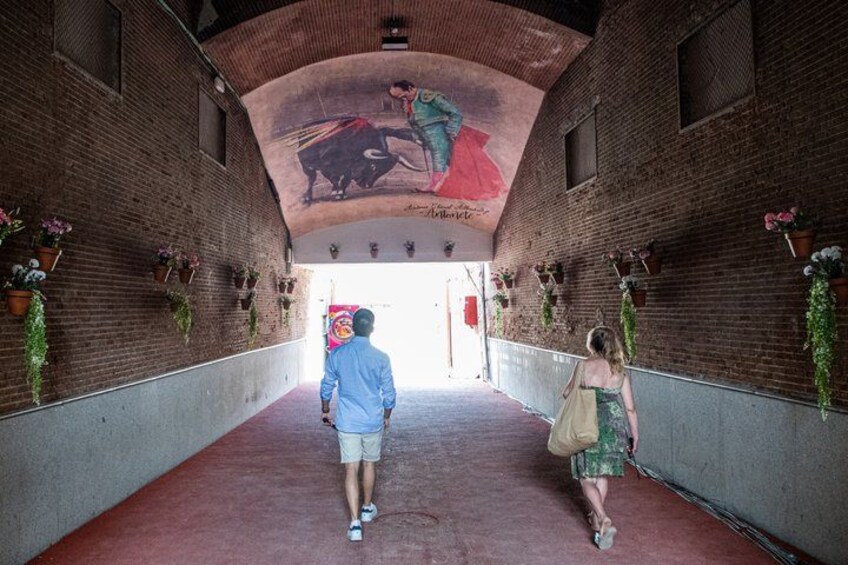 A brick corridor with hanging planters and a mural on the ceiling. 3