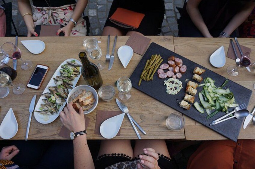 Een houten tafel met eten en drinken, waaronder een fles wijn, een schaal met zeevruchten en een plank met diverse hapjes. 3