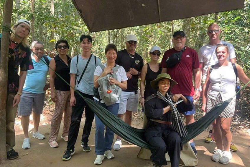 A group of people in a hammock and a shaded area with trees in the background. 3