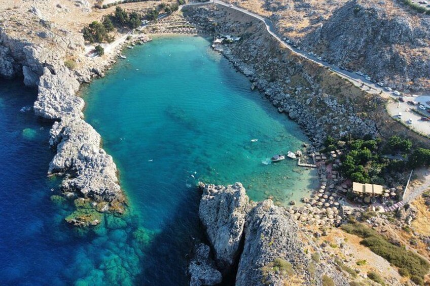A coastal landscape with clear turquoise waters, rocky cliffs, and a small settlement with buildings and a road. 2