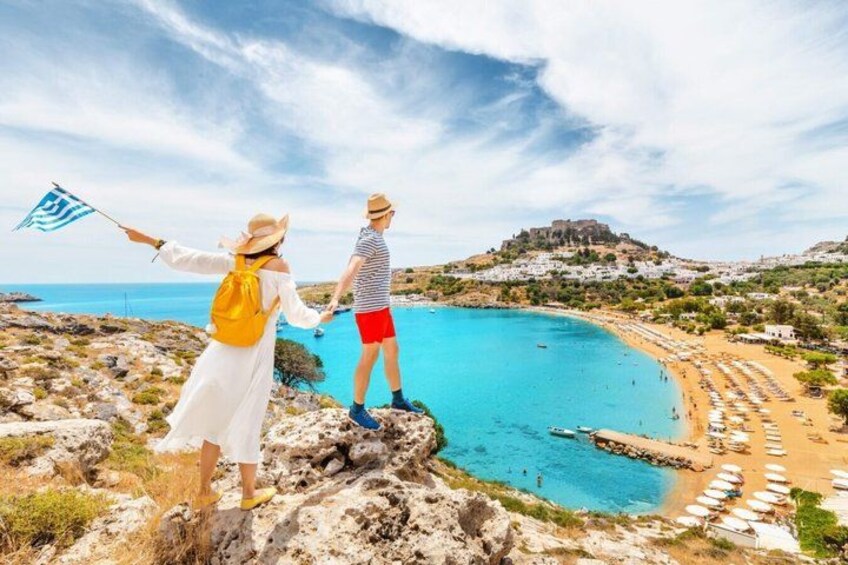 A coastal landscape with a clear blue sea, rocky terrain, and a distant hill with a fortification. 3