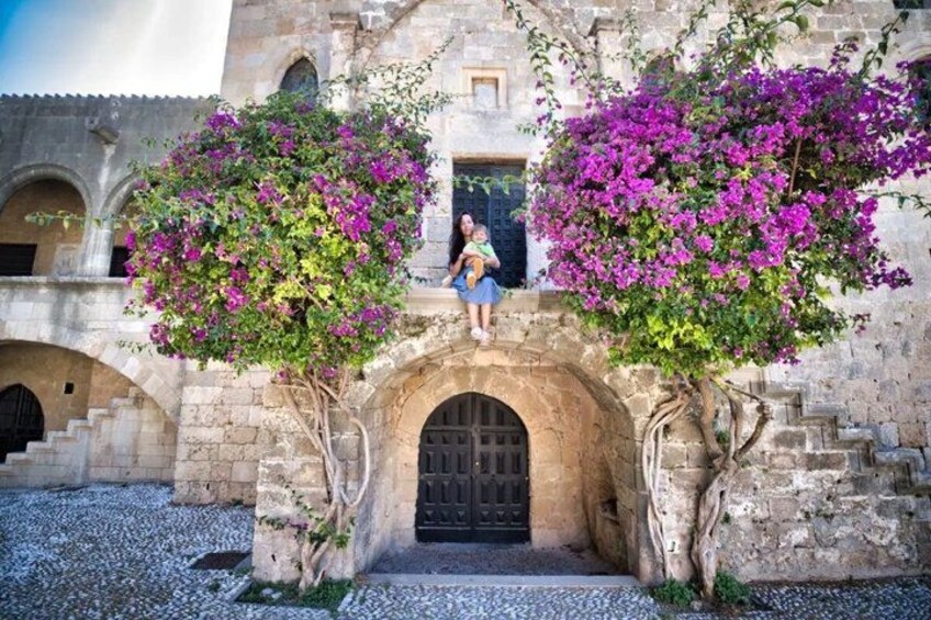 Un bâtiment en pierre doté d’arcades, une personne assise sur une corniche et des plantes de bougainvillier. 2