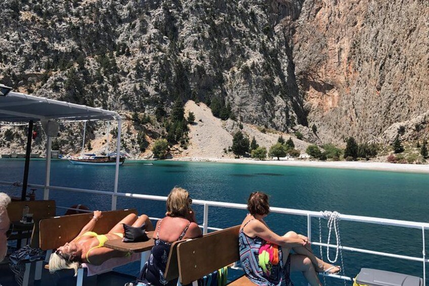 A boat with people relaxing on deck, a rocky coastline, and calm blue water. 3