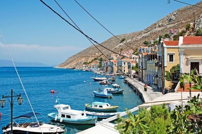 A coastal town with boats docked along the waterfront, buildings with red-tiled roofs, and a hilly landscape in the background. 5