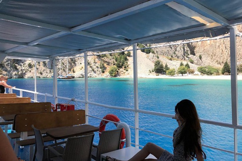A covered outdoor seating area with tables and chairs overlooking a body of water and rocky landscape. 3