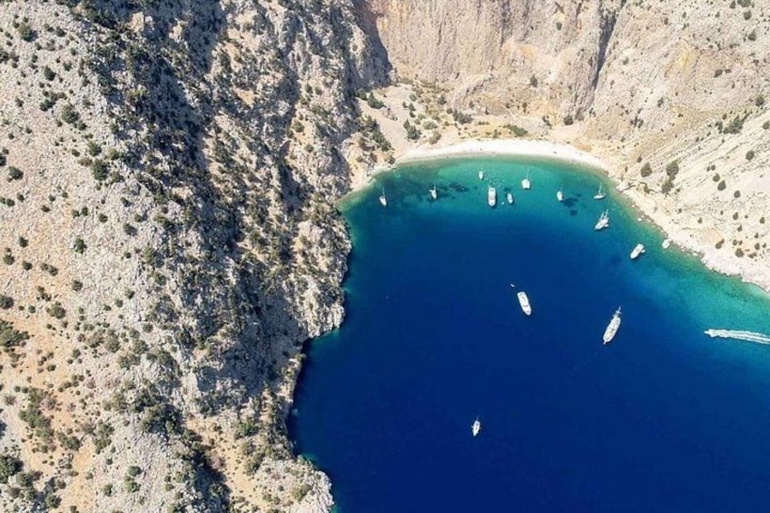 A coastal landscape with a clear blue sea, rocky terrain, and several boats anchored near the shore. 2