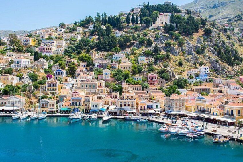 Un pueblo costero con edificios coloridos, un puerto deportivo y una ladera con árboles. 1