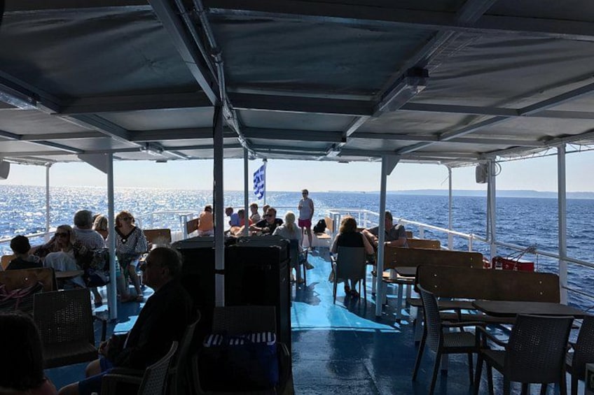 A boat with people seated at tables, a blue deck, and a view of the sea. 4