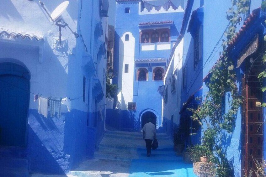 A narrow alleyway with buildings painted in blue, a person walking, and a satellite dish. 4