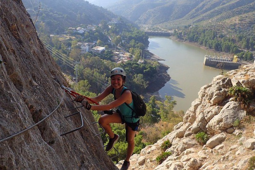 A person rappelling down a rocky cliff with a river and bridge in the background. 3