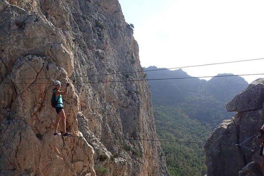 A person rappelling down a rocky cliff with a forested valley in the background. 4