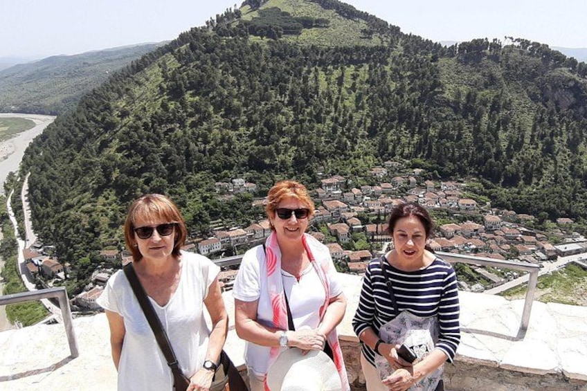 Three people standing on a viewing platform with a scenic view of a town and forested hills in the background. 1