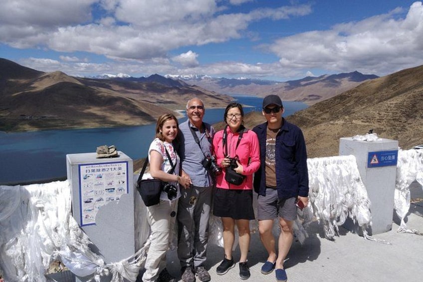 Un gruppo di persone in piedi su una piattaforma panoramica con un paesaggio montuoso e un lago sullo sfondo. 4