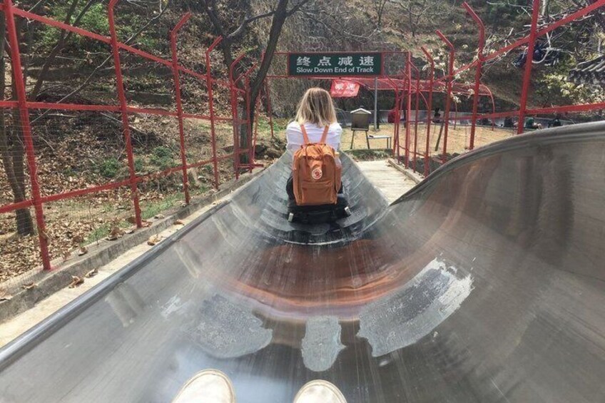 A person sliding down a track with a red fence and trees in the background. 3