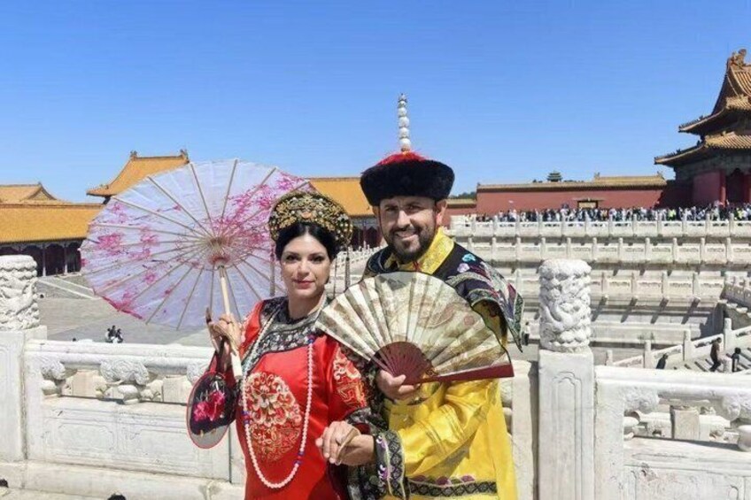 A person in traditional attire holding a fan and a decorative umbrella, standing in front of a historical building with a golden roof. 5
