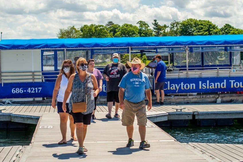 En træbrygge med folk, der går hen mod en blå båd med teksten 'Clayton Island Tour'. 2