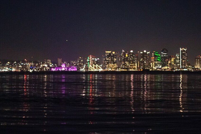 A nighttime city skyline with illuminated buildings reflected in the water. 2