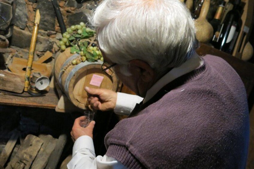 An elderly person pouring wine from a wooden barrel. 3
