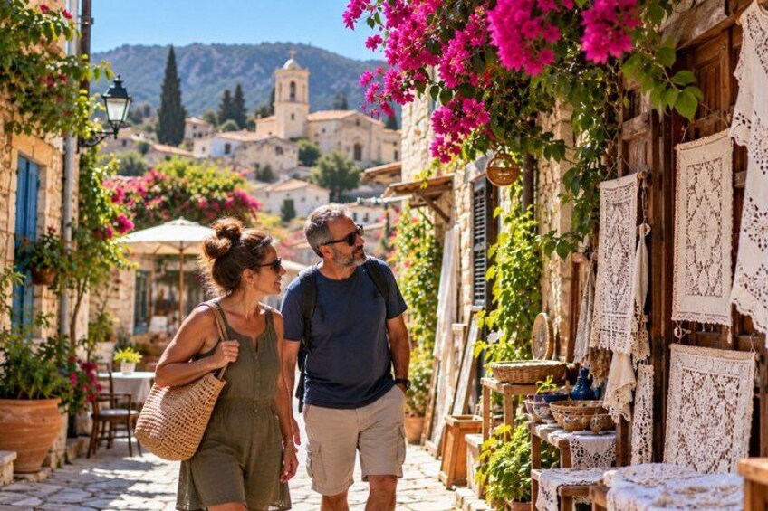 A couple walking down a narrow street with shops on either side, surrounded by flowering plants and traditional architecture. 1