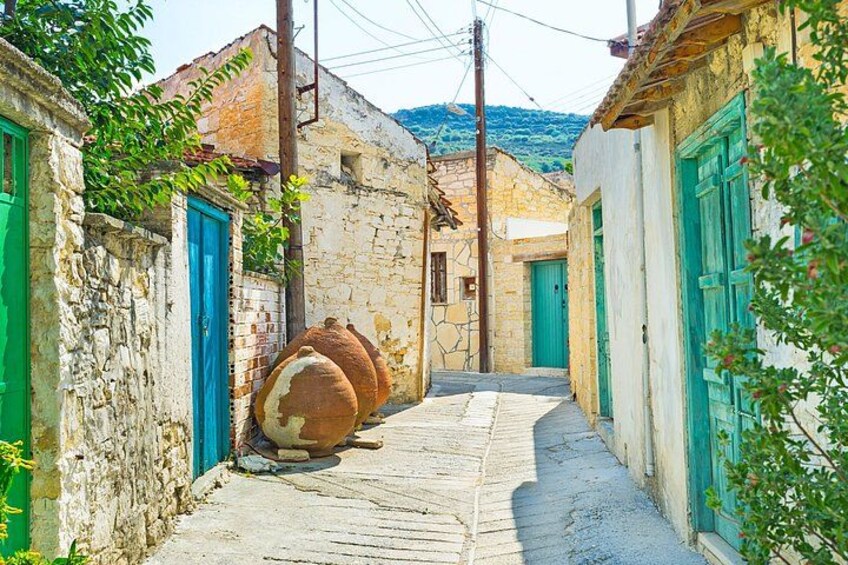 A narrow street with stone buildings, green doors, and a large barrel. 2
