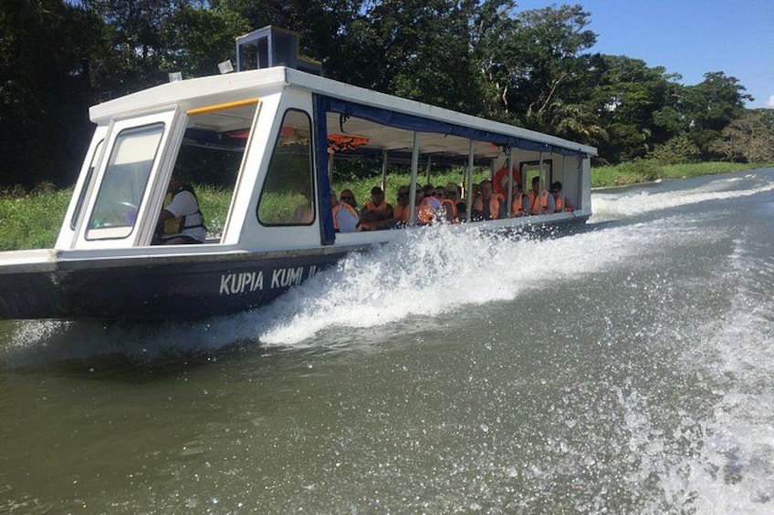 A boat named 'KUPIA KUMI' with passengers wearing life jackets, moving through a river. 1