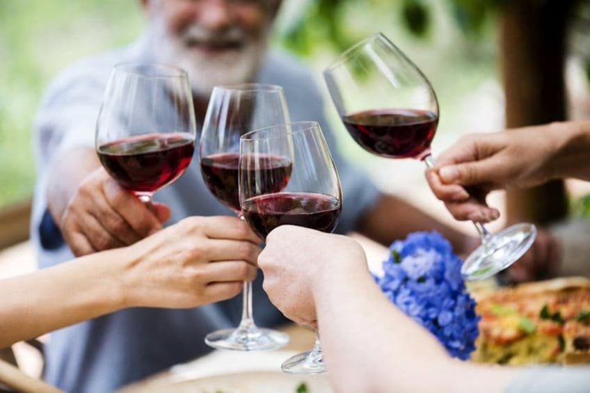 People toasting with wine glasses, a table with a dish, and a blue flower decoration. 1