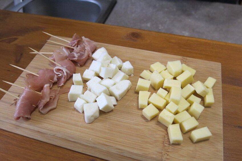 Ein Holzschnittbrett mit Spießen voller Prosciutto, Käsewürfeln und Käsebrocken. 3