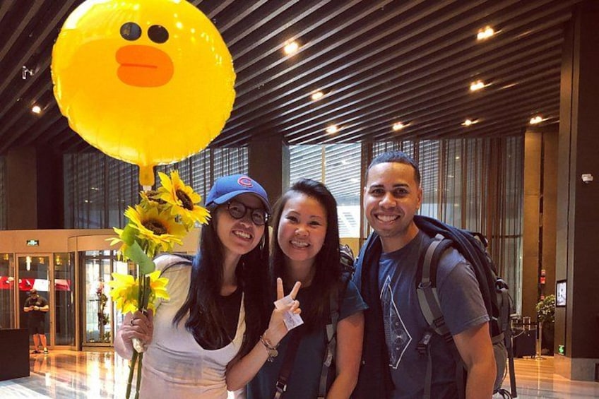 Three people in an indoor setting with a large yellow balloon and sunflowers. 2