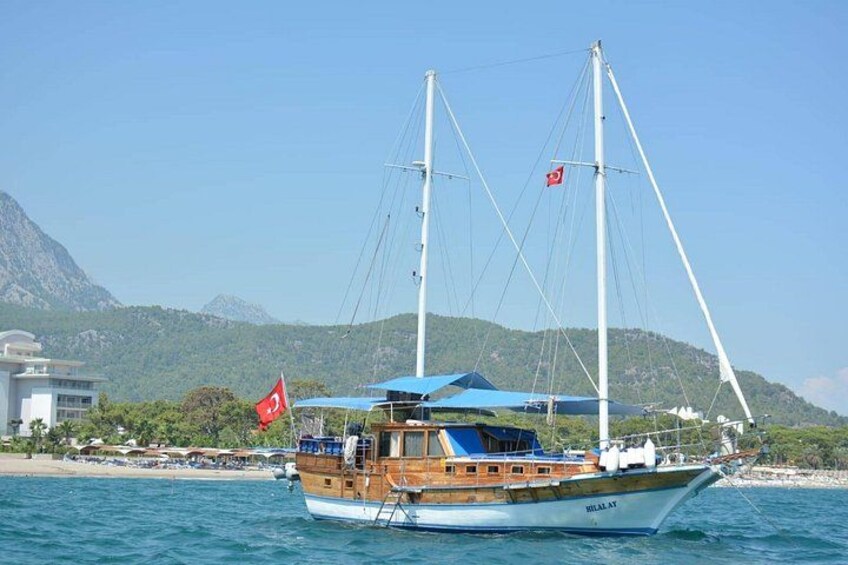 Een zeilboot met een rode vlag, een blauw zonnedek en een bergachtige achtergrond. 3