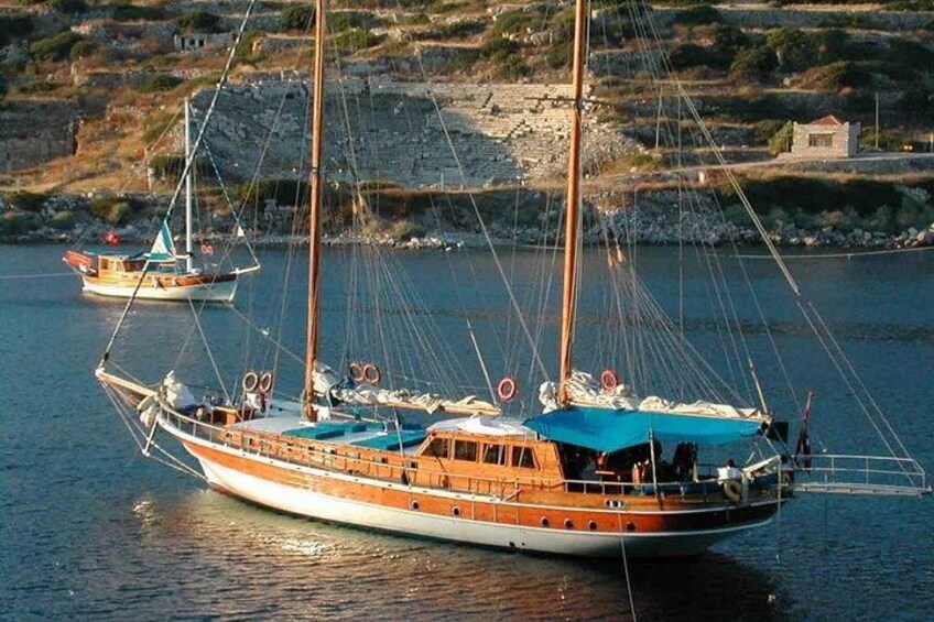 Een traditionele houten boot met meerdere masten, afgemeerd nabij een rotsachtige kustlijn, met een andere boot op de achtergrond. 5
