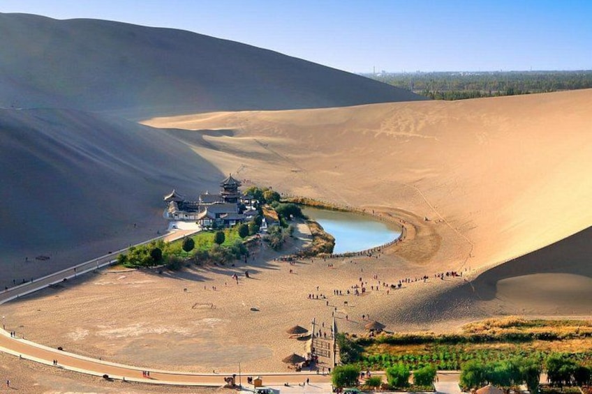 A desert landscape with sand dunes, a small lake, and a traditional building complex. 4