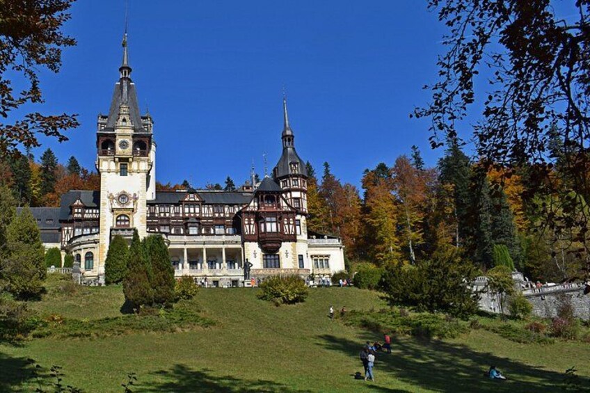 A large, historic building with two prominent towers, surrounded by a lush green park and autumn-colored trees. 1