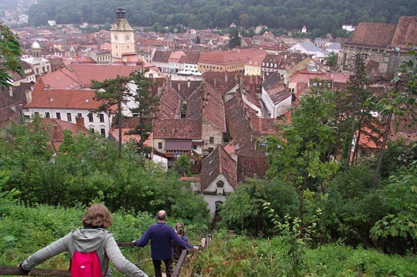 A town with red-roofed buildings, a prominent clock tower, and lush greenery. 5