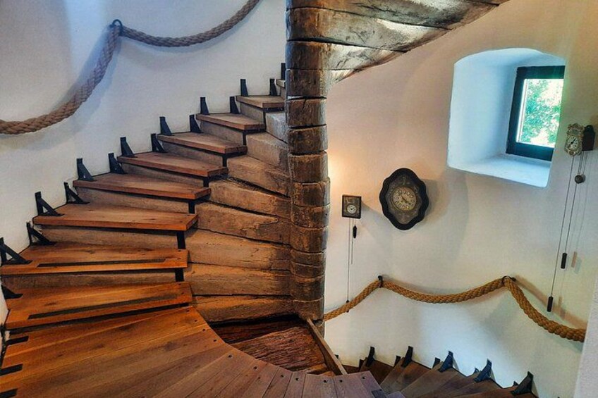 A wooden spiral staircase with a rustic design, a clock, and a small window on the wall. 2