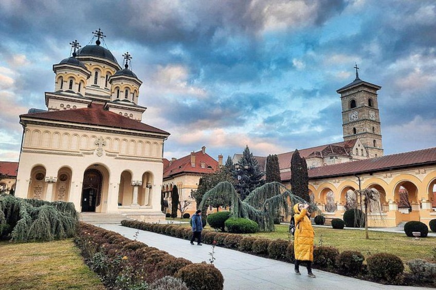 A historical building with domed towers and a bell tower, surrounded by manicured gardens and pathways. 4