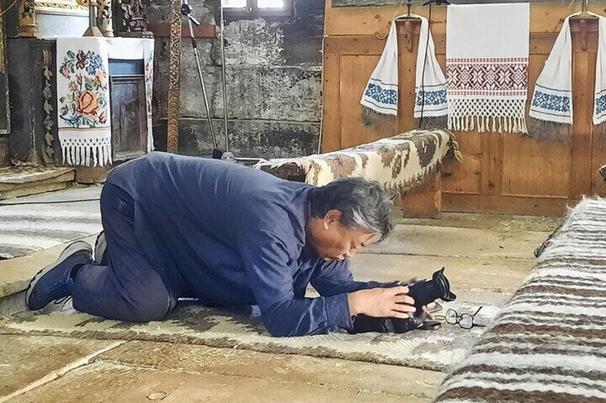 A person kneeling on a patterned rug in a room with wooden walls and traditional decor. 2
