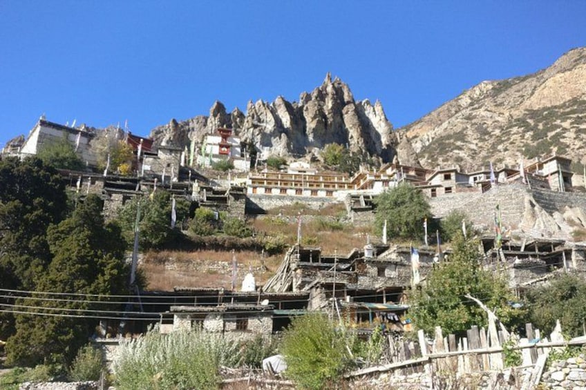 A mountainous village with traditional buildings, a prominent rock formation, and a clear blue sky. 3