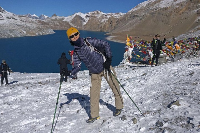 A person in a blue jacket and beige pants standing on a snowy mountain with a lake in the background. 4