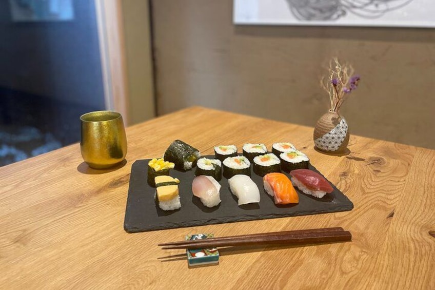Un tavolo in legno con sushi assortiti, un piccolo vaso con fiori secchi e una tazza dorata. 3