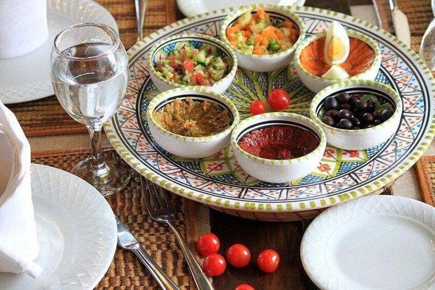 A traditional Moroccan table setting with a decorative plate holding various dishes, a glass of water, and a fork. 4