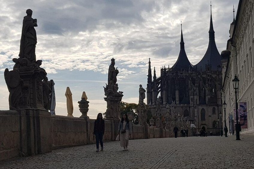 A cobblestone street with statues and a historic building with pointed towers. 2