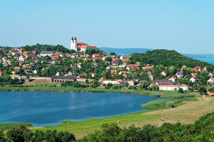 Eine Stadt am Seeufer mit einem markanten Kirchturm auf einem Hügel, umgeben von Häusern und viel Grün. 3