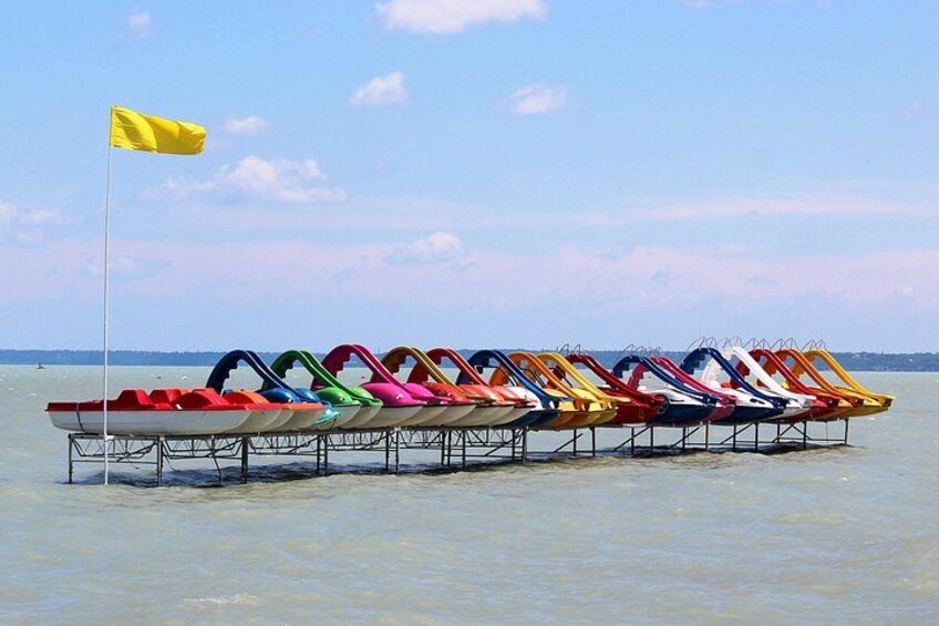 Eine Reihe bunter Tretboote liegt an einem Steg im Wasser. 4