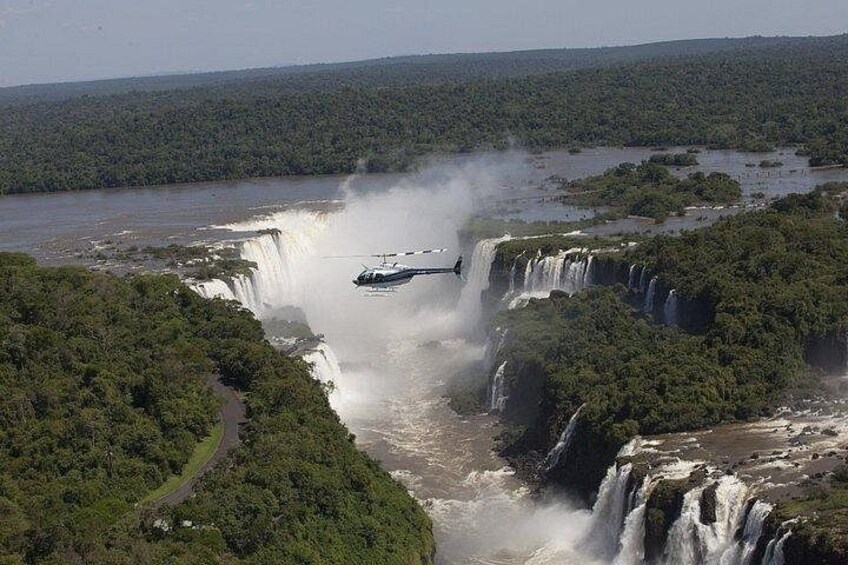 Un helicóptero volando sobre una serie de cascadas, rodeado de un bosque denso. 1