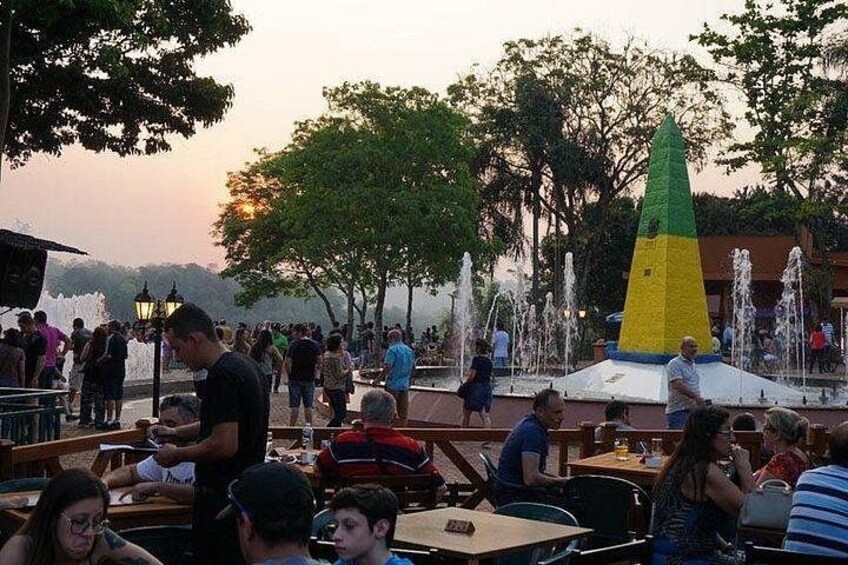 Una plaza pública con una fuente, gente cenando y árboles. 2