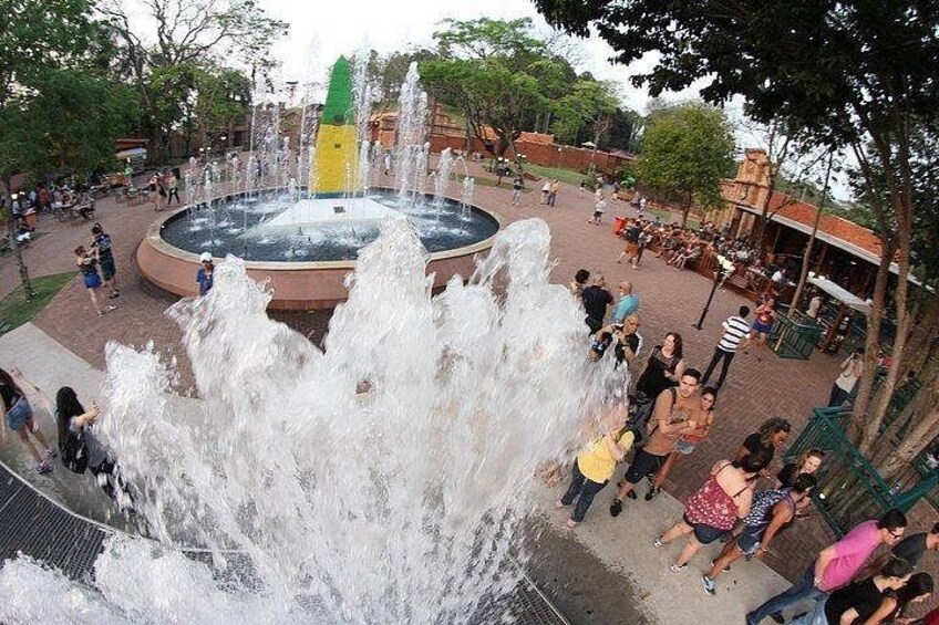 Una fuente pública con chorros de agua, rodeada por una plaza pavimentada con bancos y personas. 3