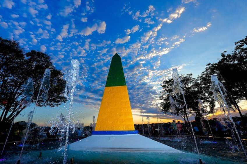 Un monument conique agrémenté de jets d’eau, entouré d’arbres, sous un ciel partiellement nuageux. 2