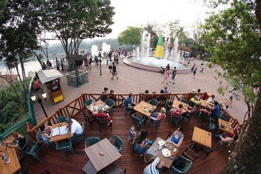 Une terrasse en bois avec des tables et des chaises, une fontaine et une vue sur l’eau. 4