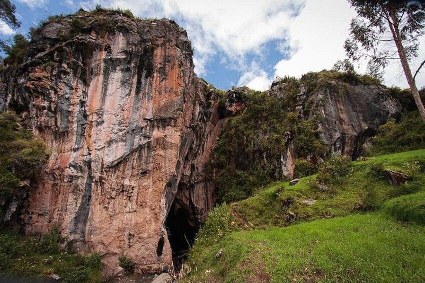 A large rock formation with a cave entrance, surrounded by greenery and a clear sky. 4