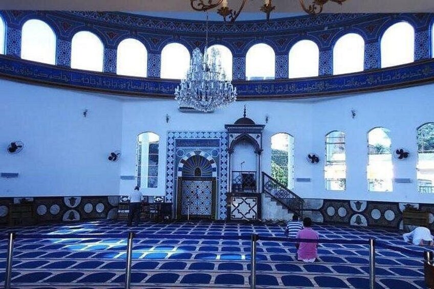 L’intérieur d’une mosquée, orné de motifs de carreaux bleus et blancs, avec un lustre et une niche de prière centrale (mihrab). 1